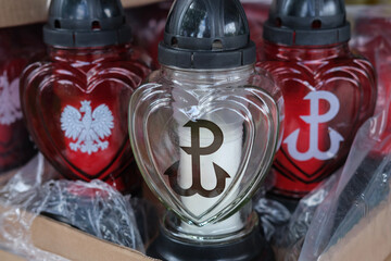 Heart-shaped grave candle with the Kotwica symbol, surrounded by patriotic red candles featuring Polish national emblems. © olga