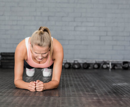 Woman performing plank exercise on rubber mat at gym studio with dumbbells and weight plates