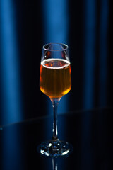 A tall glass filled with amber-colored sparkling drink placed on a reflective black surface with a dark blue background