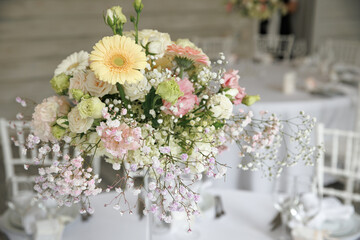 Beautiful floral centerpiece showcasing roses, daisies, and baby’s breath in a tall glass vase. Perfect for weddings or special events, adding sophistication and charm to any occasion.