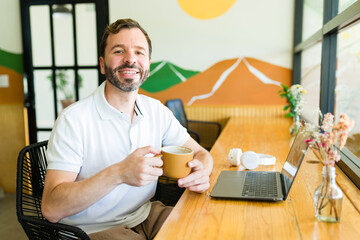 Happy freelancer working remotely in coffee shop with laptop and coffee