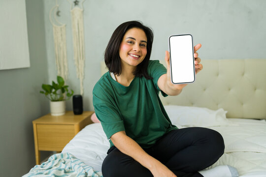 Young latin woman showing smartphone with blank screen while working from home - Powered by Adobe