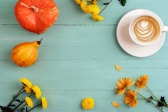 Autumn frame background of coffee cup, orange pumpkins and flowers on teal blue wooden table. Top view, flat lay, copy space