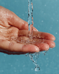 Fototapeta premium Hand cupping water droplets with sparkling blue background showcasing purity and freshness