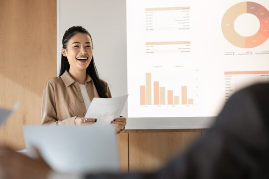 Happy presenter. Smiling young female speaker delivering successful project report to business audience colleagues investors laughing when sharing statistic data on financial growth on digital screen