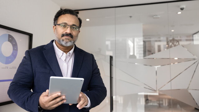 Executive decision making using digital tools. Portrait mature experienced businessman corporate leader in formal wear stand in boardroom hold tablet plan company growth using smart data. Copy space