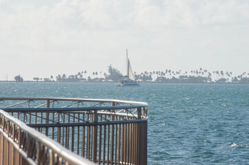 Vista panorámica de la bahía de Cataño, Puerto Rico, en un día soleado con cielo azul despejado. Un velero navega sobre el agua tranquila, reflejando la luz del sol y creando un ambiente tropical. © Caroline