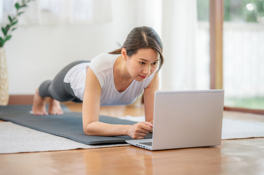 Asian woman doing plank exercise with laptop watching online lessons at home. watching fitness videos on Internet