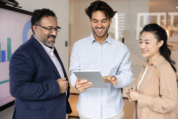 Successful insight. Three smiling businesspeople of different age ethnic background enjoy collaborative result of teamwork on tablet screen satisfied with positive financial report good business idea