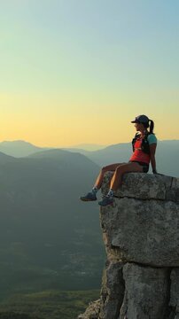 A determined female runner triumphantly sits atop a rugged cliff, overlooking expansive valleys. Dressed in athletic gear, she embodies endurance and achievement.