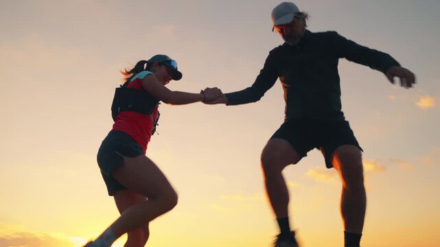Two runners, one in red and one in black, celebrate atop a rocky peak during a stunning sunset. Their high-five symbolizes triumph and camaraderie in cross-country running.