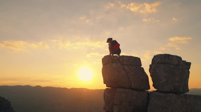 Hiker atop rugged cliff at sunset, golden sky and distant mountains, symbolizing achievement, reflection, endurance, and joy in the great outdoors.