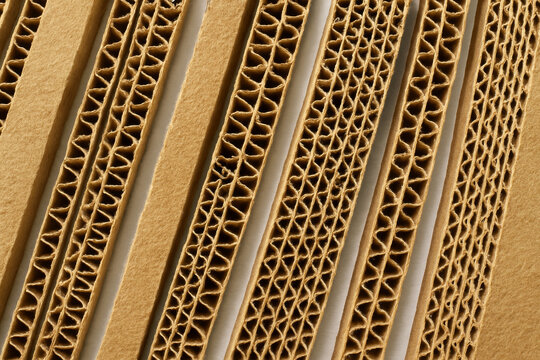 Close-up of corrugated cardboard strips arranged in diagonal pattern, showing wavy inner fluting texture and layered construction for packaging material or sustainable product background