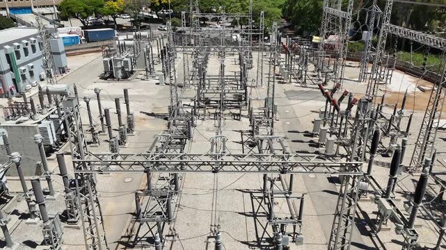 Aerial drone view of an industrial electrical substation with transformers and high-voltage power lines. Infrastructure of the national power grid, captured from above.

