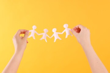 Woman holding paper figures of people on orange background, closeup