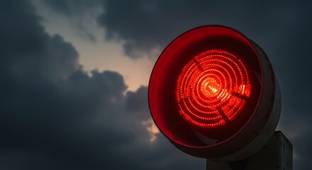 An illuminated red warning light glows brightly against a dark, dramatic, and cloudy sky.