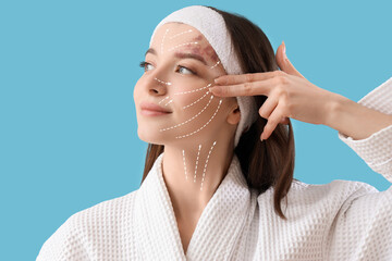 Young woman in bathrobe doing face building exercise on blue background, closeup