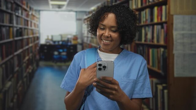 Woman smiling holds smartphone with one hand among tall bookshelves in building with studious expression; serenity.