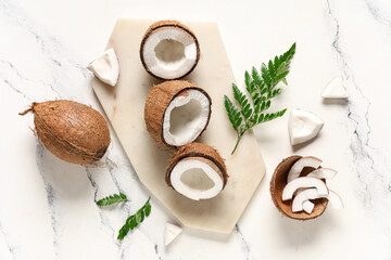 Board with halves of fresh coconuts and leaves on white background