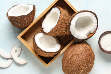Wooden box with fresh coconuts and bowl of flakes on light blue background