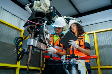 Fototapeta premium Two people are working on a machine. Diverse team of male and female engineers collaborating on the maintenance and programming of a welding robot in a factory.