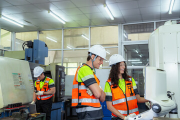 Three people are working in a factory. Group of machinists in an on-the-job training session, learning to program and control an automated industrial machine.