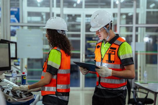 Two people wearing safety vests and hard hats. Team of diverse engineers having a discussion and planning with a clipboard before operating machinery in a factory.