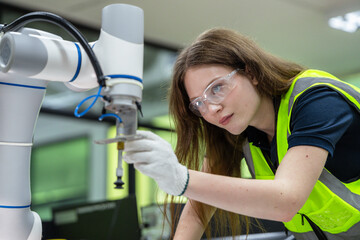 A woman wearing a yellow vest is working on a robot. Robotics engineer specializing in maintenance, carefully inspecting and adjusting the tooling of a modern robotic arm.