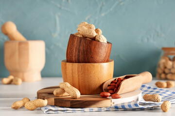 Bowls with fresh peanuts, scoop and napkin on light wooden table