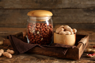Tray with jar and bowl of peanuts on wooden table