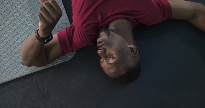 Finishing rep African American man stretching hamstrings on gym floor and preparing next move