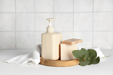 Composition with bottle of shower gel, soap bars and towel on table near beige tile wall
