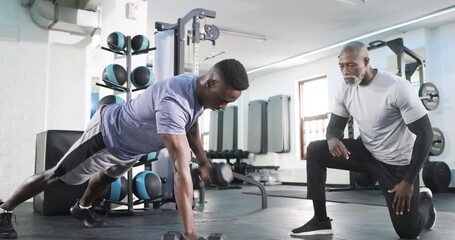 After trainer cues, African American man performing renegade dumbbell rows at gym building strength - Powered by Adobe