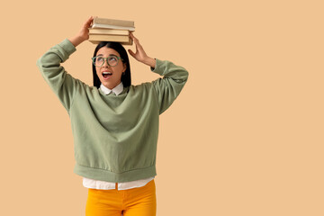 Beautiful woman in eyeglasses with books on beige background