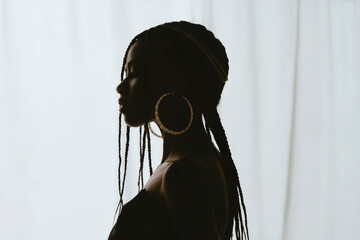 A high-contrast artistic portrait photograph of a Black woman in profile view, facing left against a pure white background.