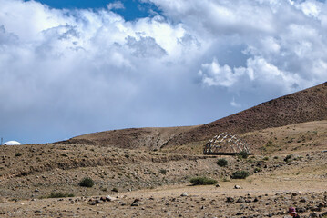 A wooden dome structure stands in the arid landscape under a cloudy sky.