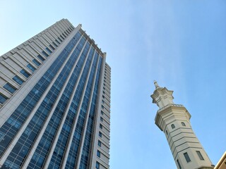 Skyscrapers and mosque minarets next to them with a bright blue sky in the background.