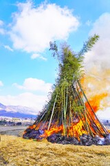 青空背景で正月飾りや書初めを燃やすどんど焼きの大きな櫓、新年の無病息災を願う日本の熊本の正月の風景
