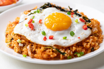 Korean kimchi fried rice with fried egg, pork, sesame seed, chili, spring onion and seaweed on white plate