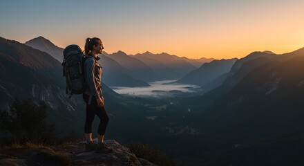 Fototapeta premium A woman hiker stands atop a mountain ridge, gazing at the valley below during sunrise.