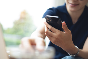 Happy relaxed young woman sitting at home, using smartphone for checking social media or online shopping. Asian woman enjoy doing e-commerce shopping or video call with friend via mobile phone
