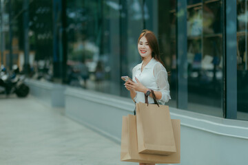 Happy Asian woman shopping with ease, holding her purchases and smiling brightly — a simple moment of weekend relaxation and lifestyle.