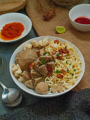 Delicious bowl of chicken noodle soup with meatballs, vegetables, and sambal. Traditional Indonesian comfort food.