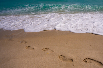 Turquoise sea water wave motion. Foot steps on sand. Calm sea. Seaside resort. Bright sky and waves on beach. Beautiful foamy shoreline. Sea background. Blue ocean. Sandy ocean beach. Sea waves.