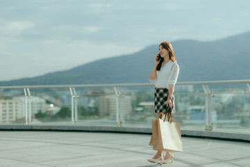 A joyful Asian woman holds a shopping bag with grace and charm, her bright smile reflecting a delightful shopping moment.