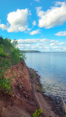 Scenic view of a tranquil lake surrounded by lush greenery and rocky shoreline under a bright blue sky with fluffy clouds reflecting on the water surface