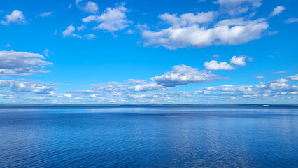 Expansive view of tranquil blue ocean under a bright sky filled with fluffy white clouds, reflecting sunlight on the water surface, creating a serene atmosphere for relaxation