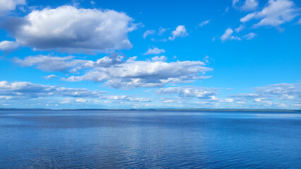 Expansive view of tranquil blue water reflecting fluffy white clouds under a bright blue sky, creating a serene and peaceful atmosphere in nature's beauty