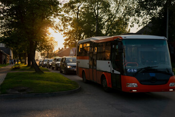 Fototapeta premium City bus and line of cars in residential neighborhood during golden hour, evening urban transportation scene with warm sunlight for traffic, public transit, mobility or commute concepts