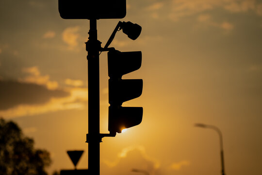 Silhouette of traffic light and surveillance camera at sunset with golden sky in background, urban street safety and transportation concept for traffic control, monitoring or city life themes